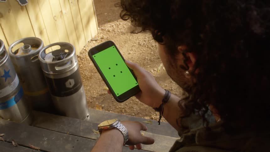 Man with curly hair earrings and a silver wristwatch looks down at smartphone