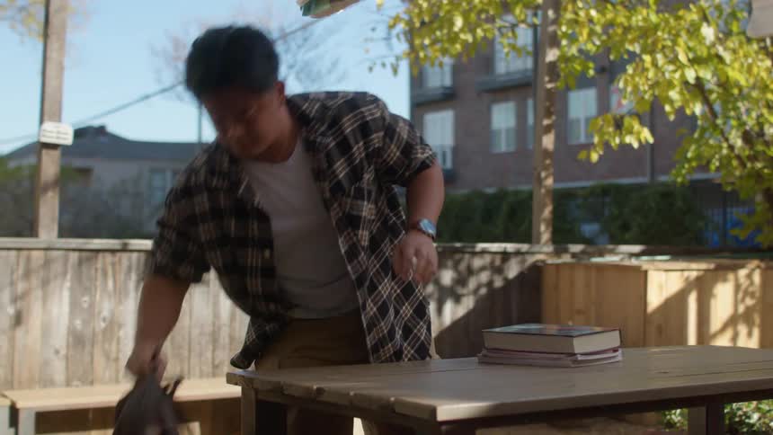 Man rising from an outdoor table and packing his notebooks and books into a backpack