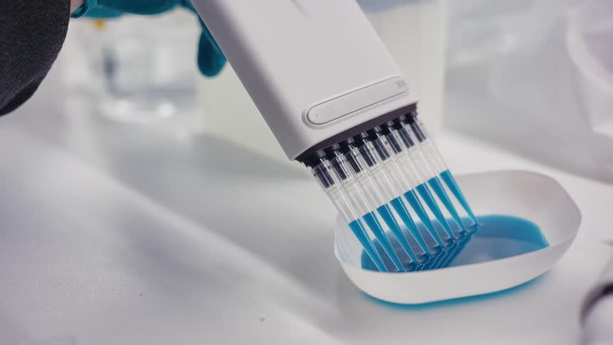 Scientist uses multisyringe tool to suck up blue liquid from a bowl