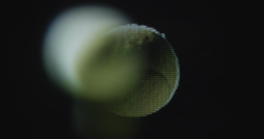 A digitized yellow tennis ball rolls or spins in the air on a computer screen with visible pixels and distortion as it warps and fades with black or dark background