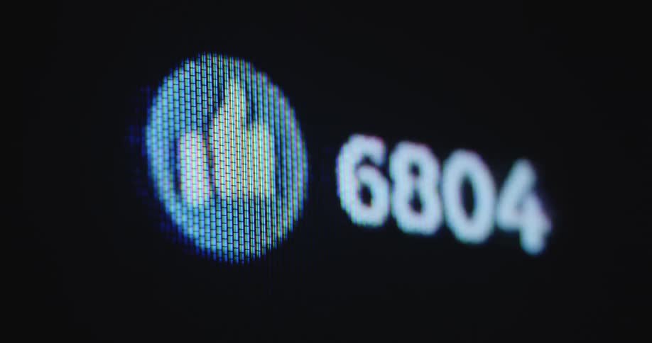Extreme macro closeup of a black digital screen from a vintage computer with a blue thumbs up symbol and white numbers increasing alongside in a very fast and positive way