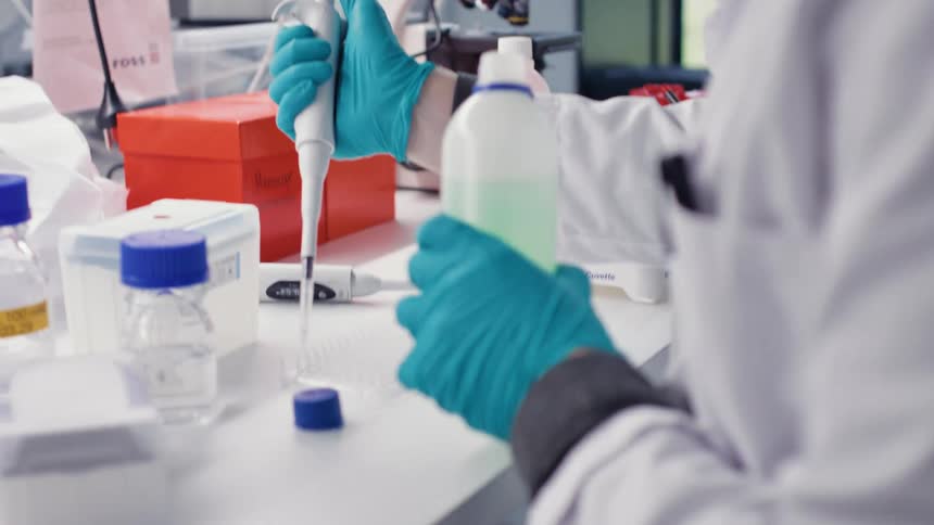 Closeup of a womans gloved hands extracting liquid and placing it in a laboratory vial