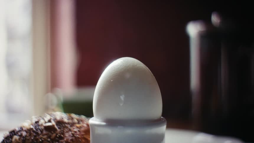 A person cracks the shell on a hardboiled egg with a spoon