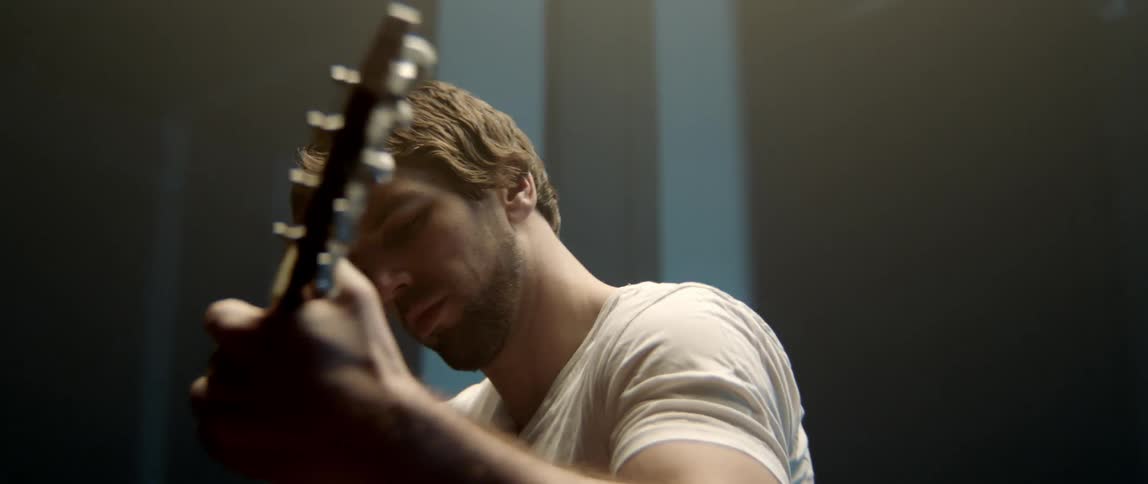 A man playing a wooden acoustic guitar with focused emotional expression.