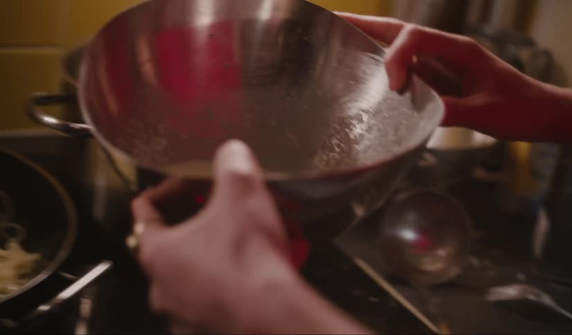 Chef stirs fettuccine sauce and pours it over noodles in a pant in a yellow kitchen