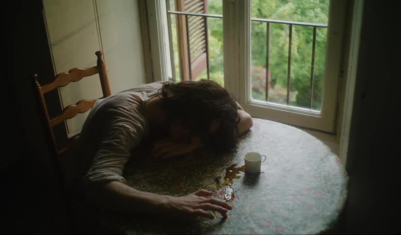 Tired man with long hair and white t shirt sits at table