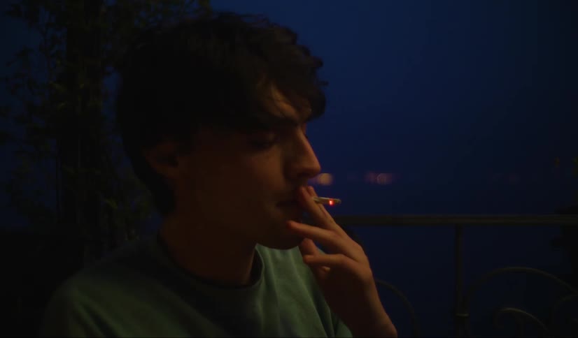 Young man smoking near a window at night