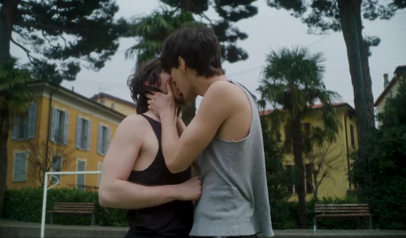Male couple make out on sports court surrounded by buildings and trees