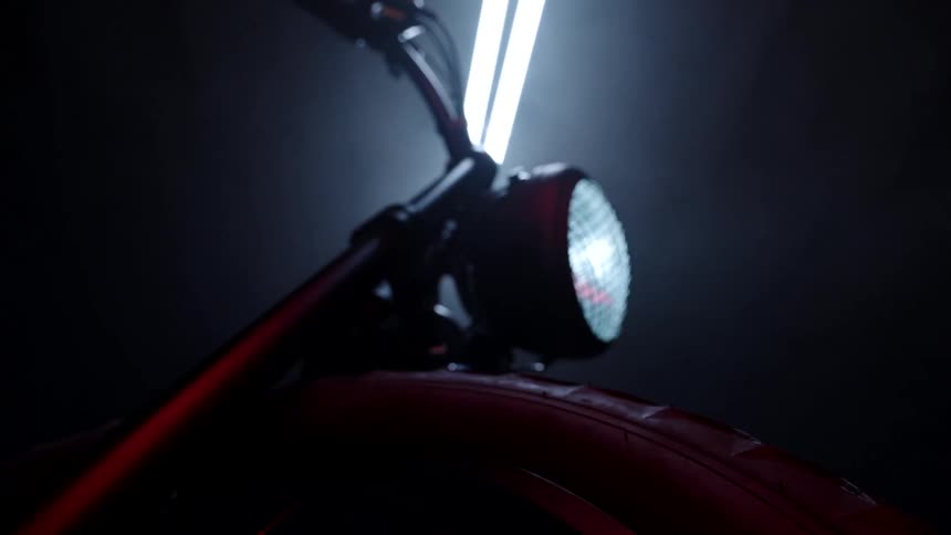 The headlight of a motorcycle is on as the camera pans down past its front wheel