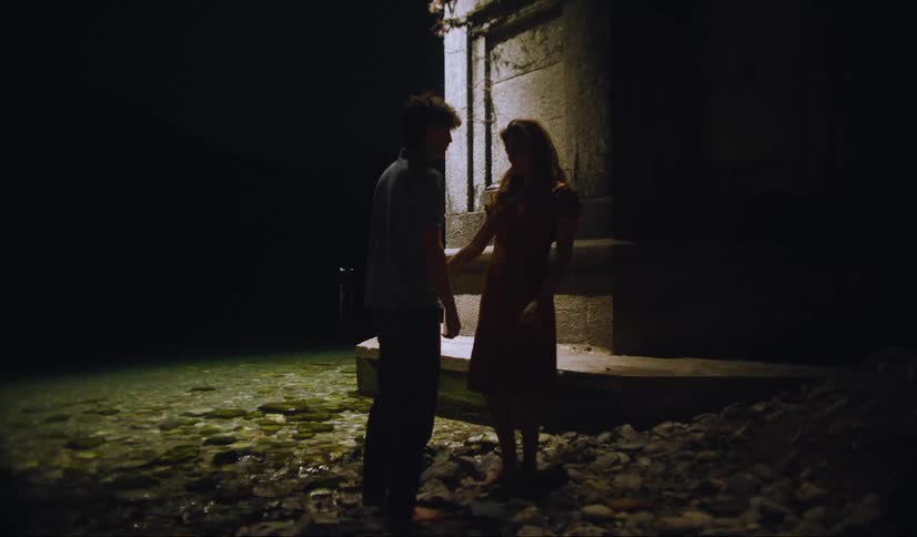 Couple stand on the rocks next to the shallow water and talk in the darkness