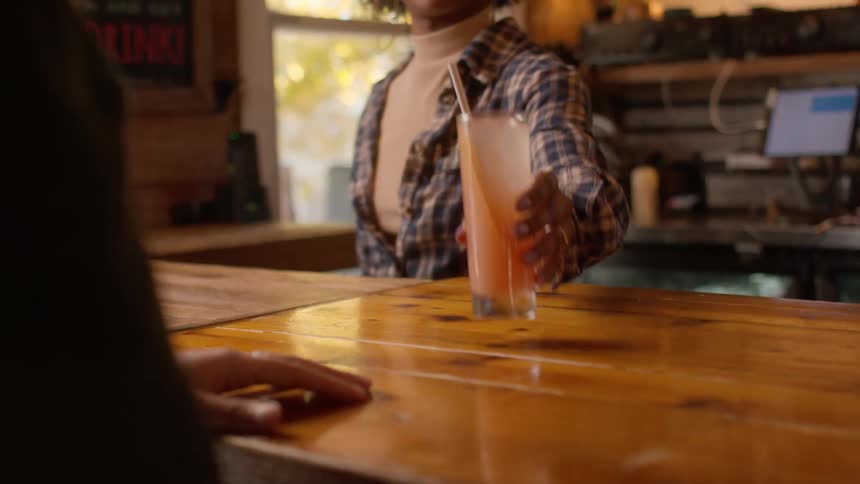 Black woman hands beverage to person across counter