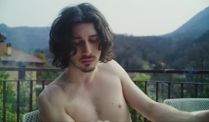 Young man reading and smoking on a balcony near the mountains