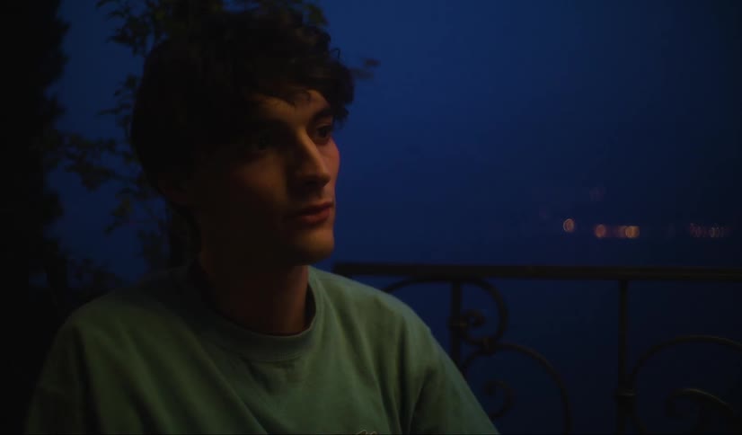 Man watches intently and lifts his head slightly with lights sparkling in the water behind him