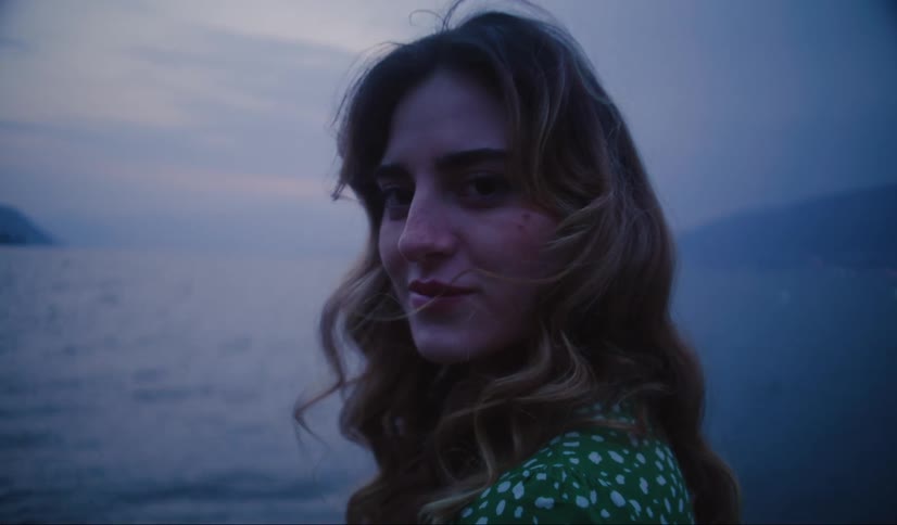 A woman with long wavy hair stands overlooking the ocean