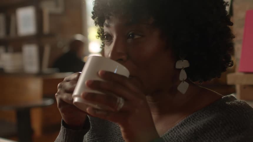 Woman nods after taking sip of coffee while sitting in restaurant