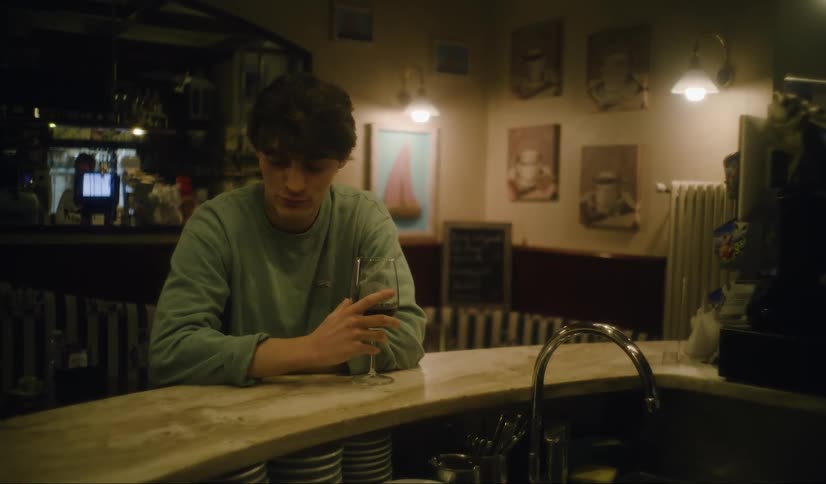 A nervous man sits alone at a bar and guzzles down a glass of wine