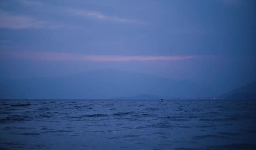 Water ripples and waves as a boat sails and lights glow along the coast