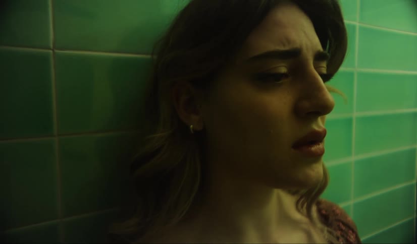 A woman is sad and breathing deeply while leaning against a green tiled wall