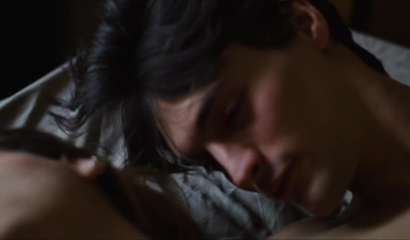 A man kisses the neck of a woman while she is sleeping next to him on the bed