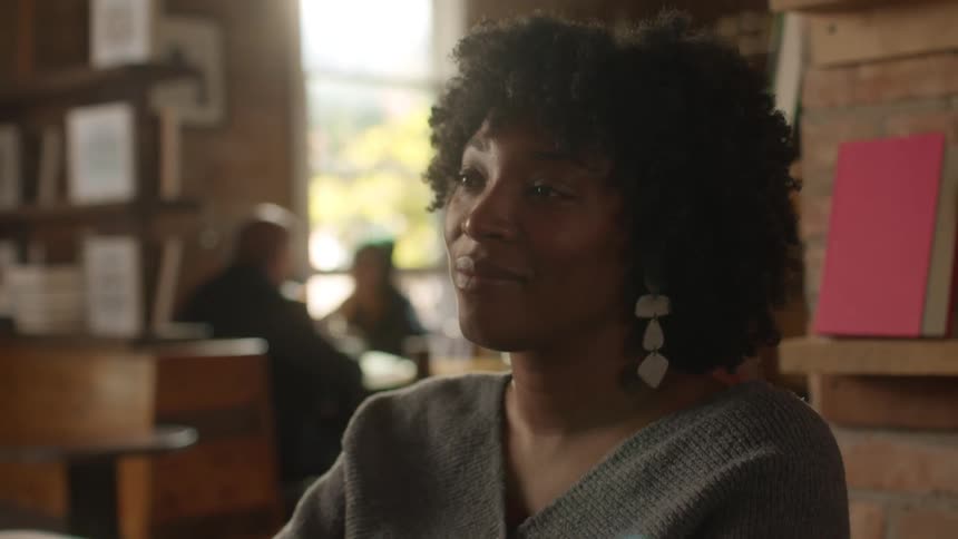 Black woman sits indoors nods and looks intently at someone
