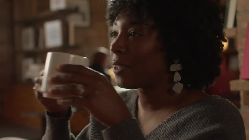 Lady sits in a bar at midday drinking from a mug and smiling