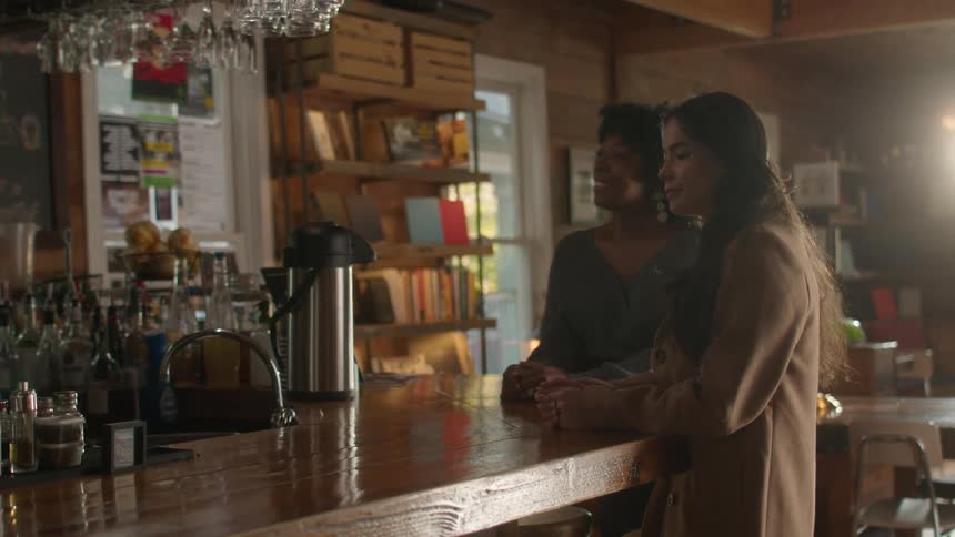 Two women walk up to the bar counter and one uses her phone