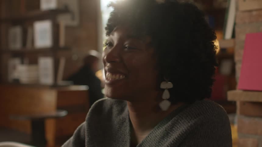 A woman smiles and nods while talking to someone at a coffee shop