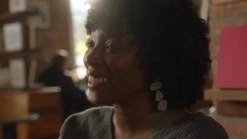 Lady sits in a bar talking while shaking her head with a mug in her hands