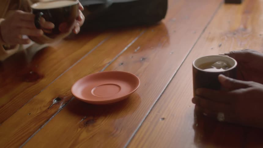 Seated at a cafe table women smile and enjoy friendly conversation each holding a cup of coffee
