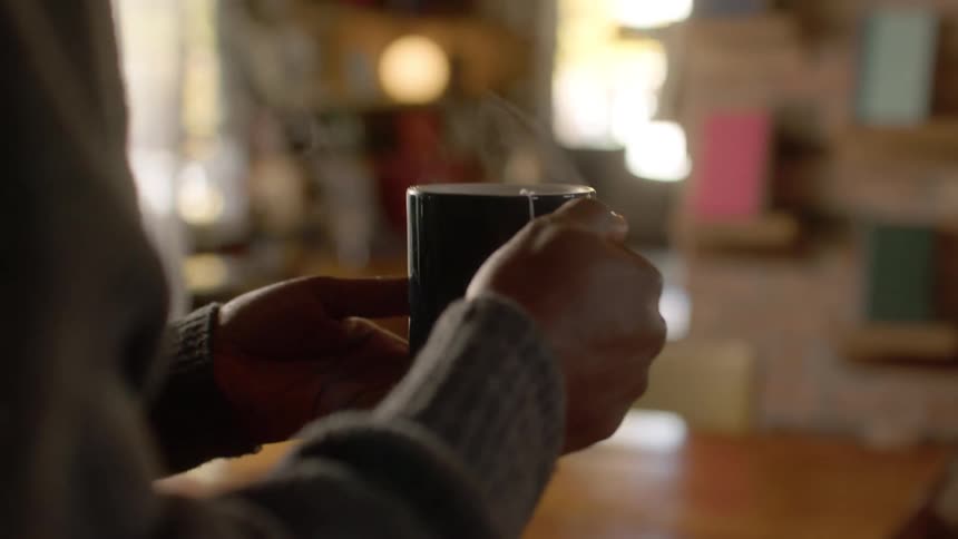A steaming cup of tea is carried to a table where a woman is already seated