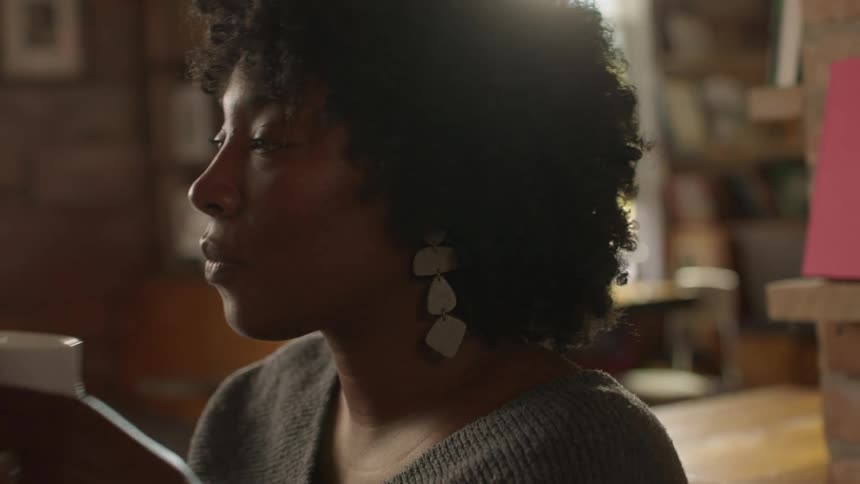 A woman sits in a cafe sipping from a mug and agreeing with someone in conversation