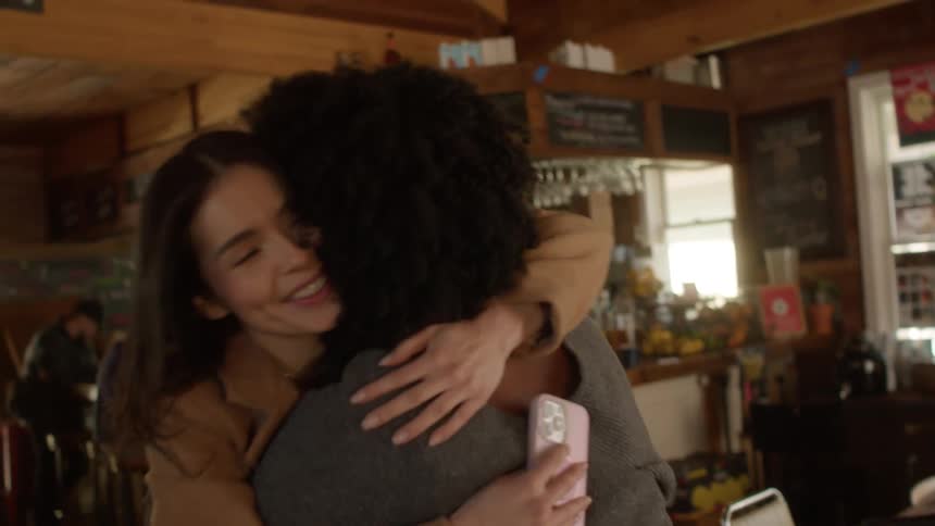 Friends greet each other with a hug on a coffee shop