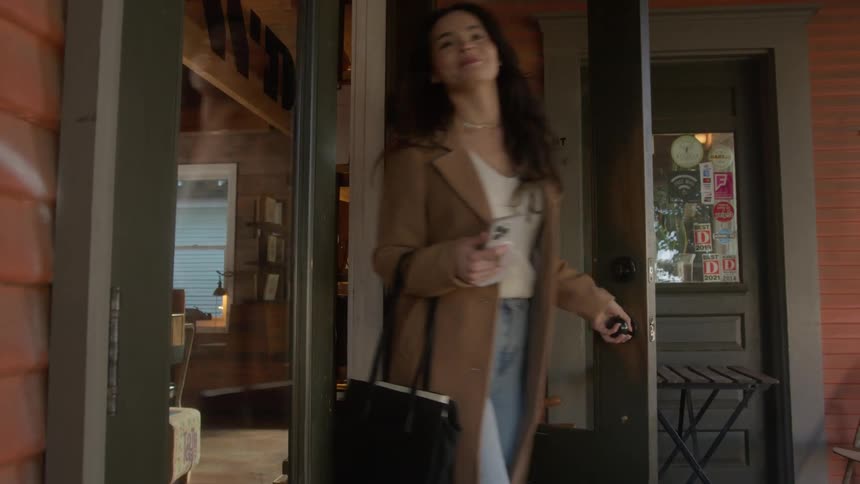 Woman exits the shop carrying a black purse and holding a phone in her hand