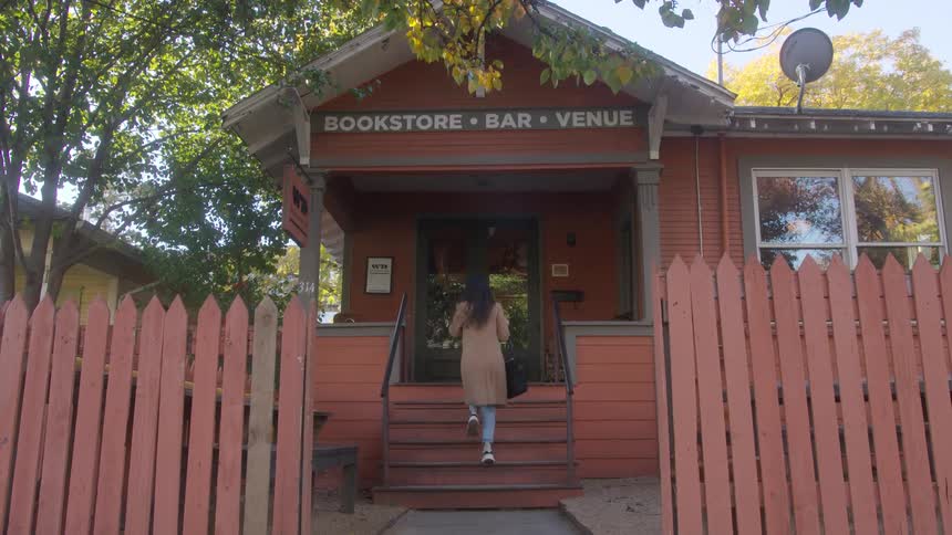 Lady walks inside a bookstore at midday with a mobile phone held to her ear