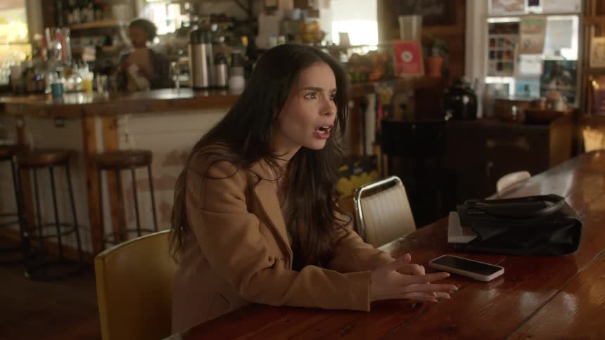 Brunette woman sits at table indoors checks watch while having conversation