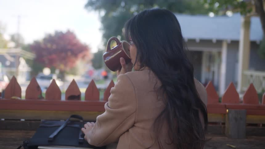 A woman sitting in an outdoor coffee shop drinking a cup of coffee