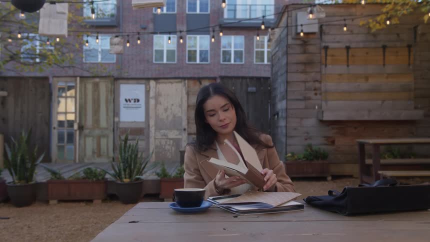 Brunette woman sits at a table and opens book