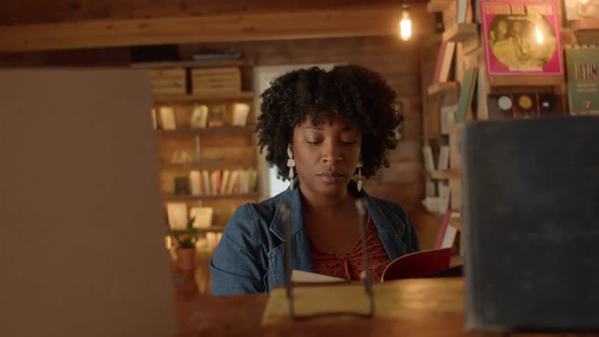 A young woman takes a book from a shelf and begins to read it