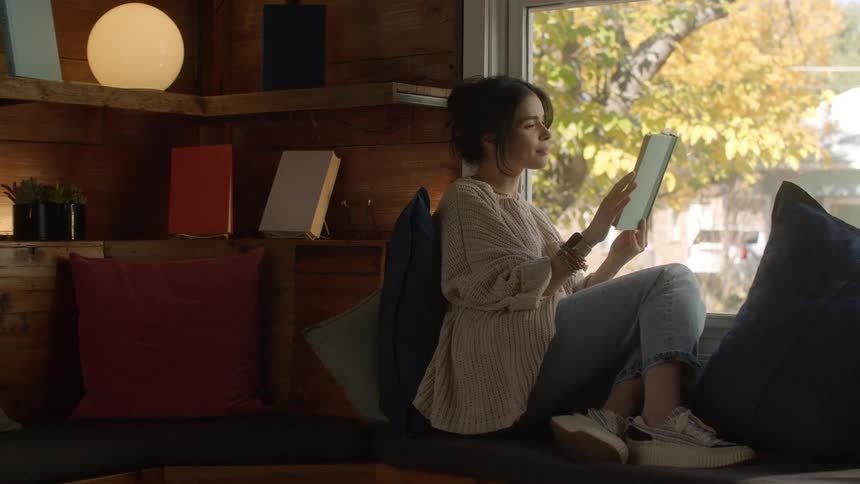 Woman sits near house window reading a book in the fall