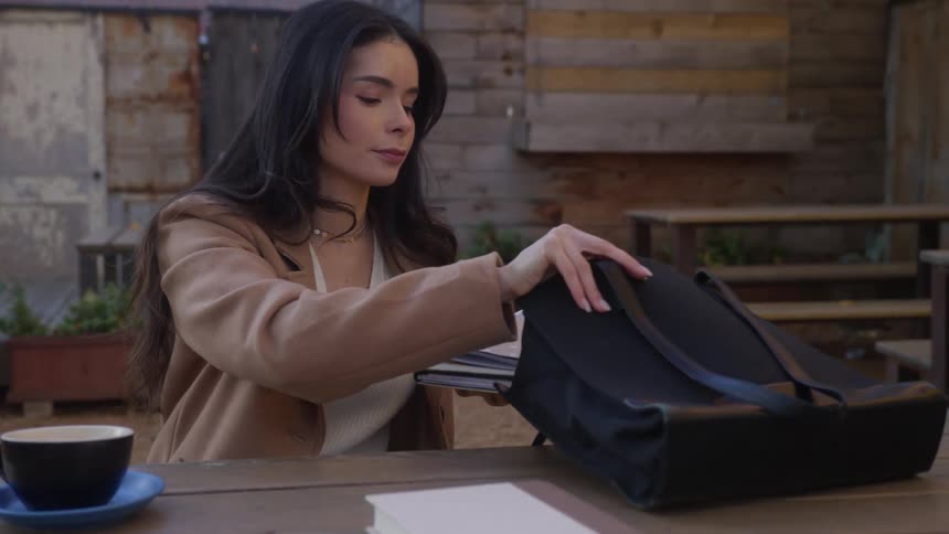 A woman putting files into her bag while sitting on a cofee table