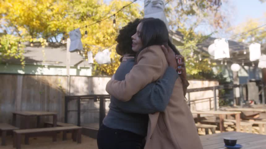 Friends greet each other with a hug in an outdoor backyard dining area on a fall day