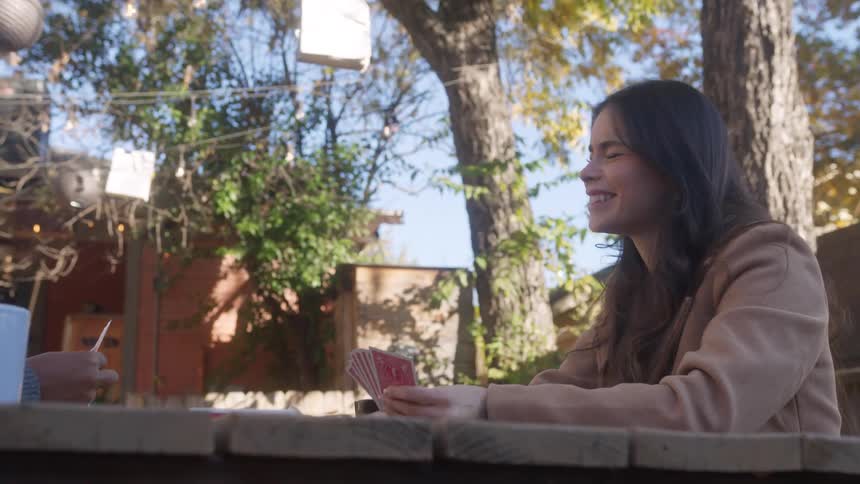 Woman playing cards with her friend at the picnic table in the backyard on a sunny day