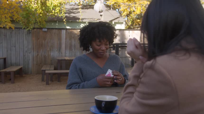 Women seated at a table in the cafe yard share smiles and engage in conversation with each other