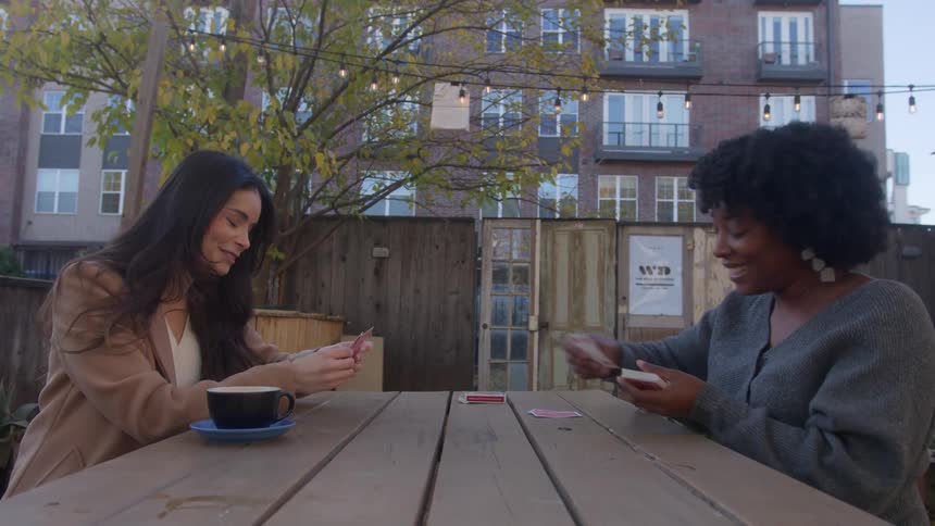 Friends play card game at picnic table with apartment building in the background