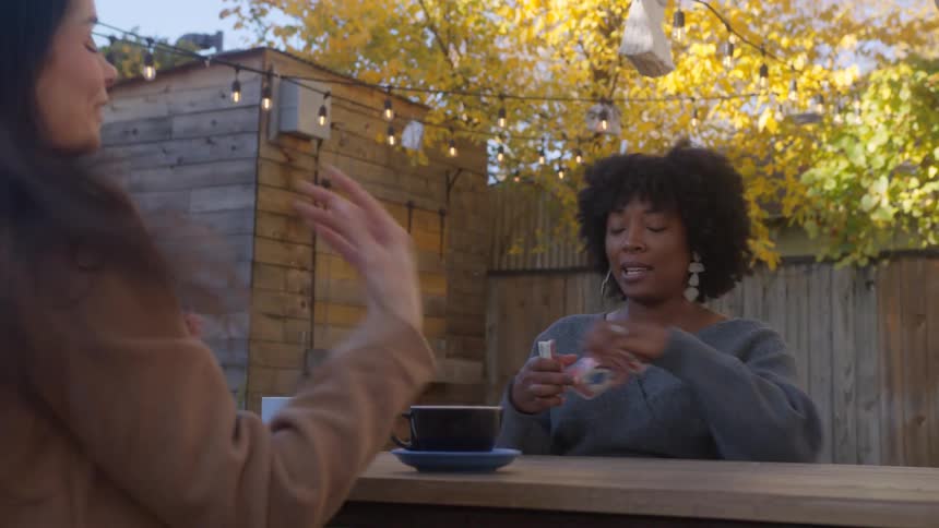 Seated at a table in the cafe yard women share smiles engage in conversation and enjoy a card game together