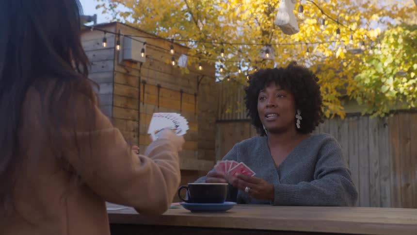 Two females playing cards while seated in the yard at midday