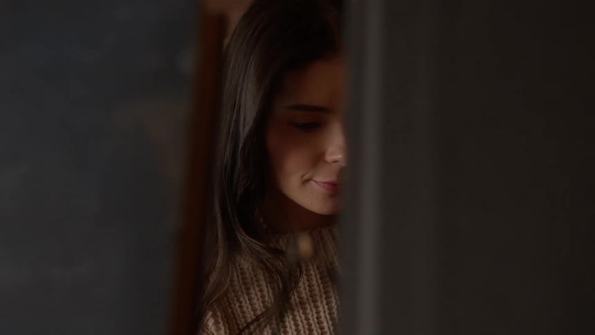 A young woman behind some objects looks down and gives a small smile