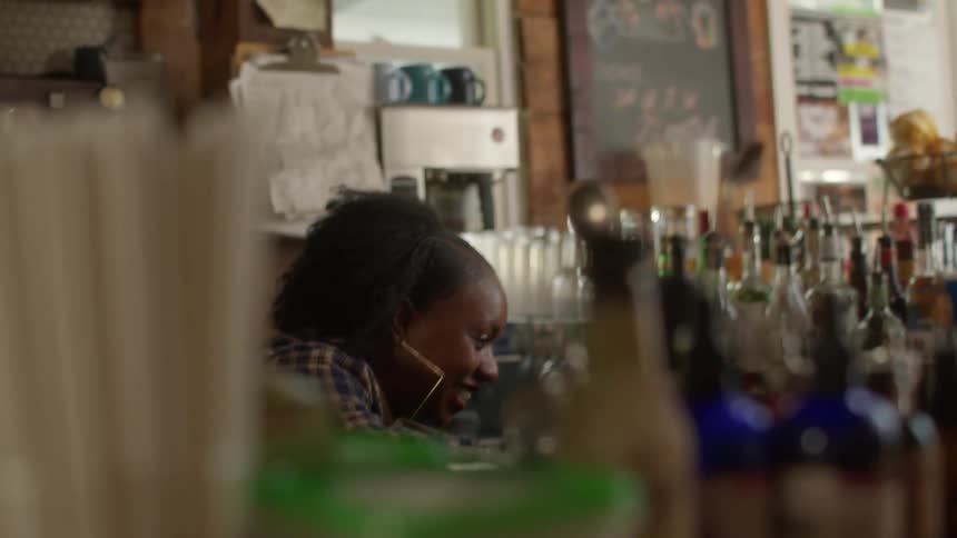 A woman barista stationed behind the counter engages in conversation and shares laughter with someone