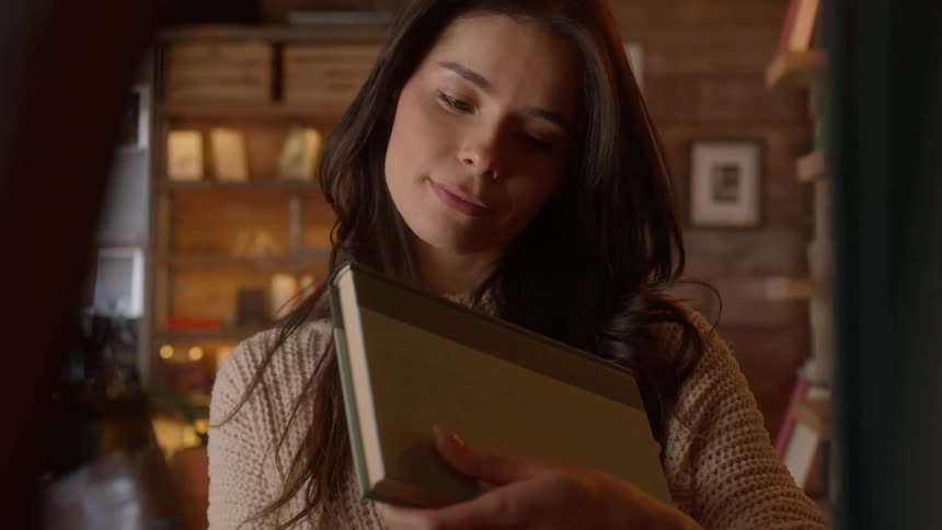 A woman smiling as she selects a book from a shelf in a bookstore or library