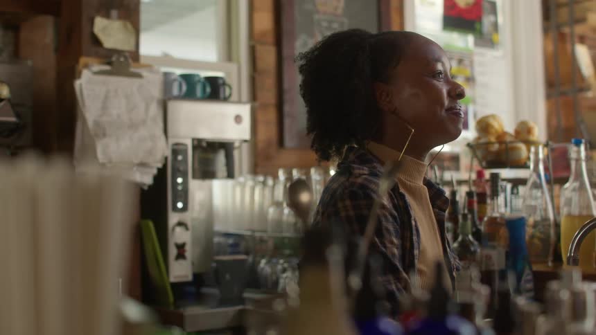 A woman barista stationed behind the counter engages in conversation and shares laughter with someone